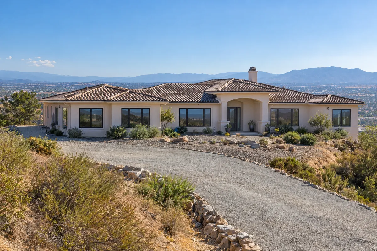 Hilltop ranch home with a tile roof, dark-framed windows and a gravel perimeter above a valley